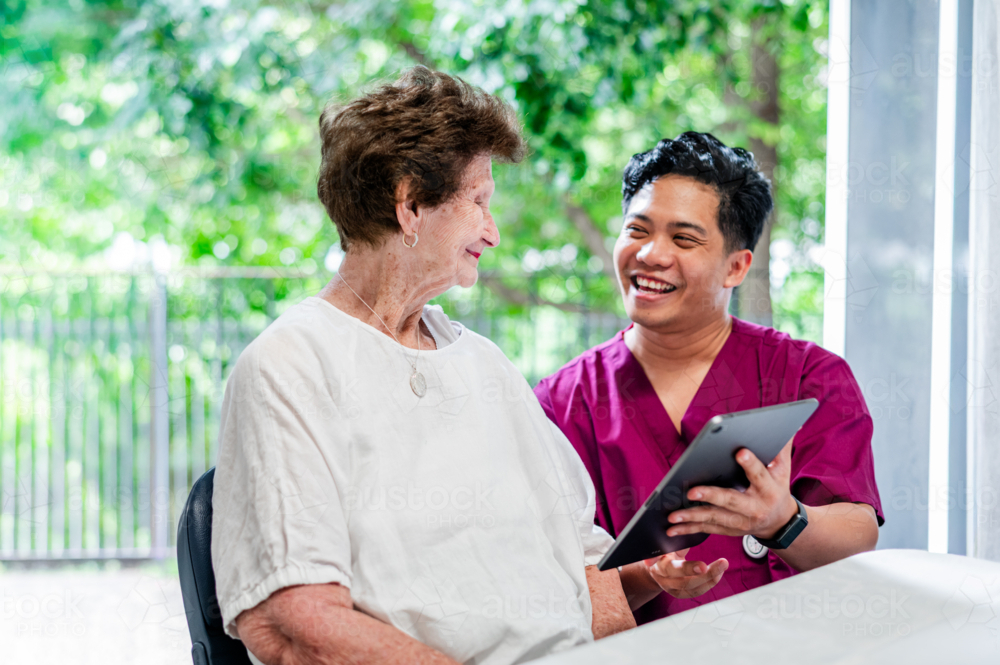 Healthcare worker showing health records using tablet device to an elderly woman - Australian Stock Image
