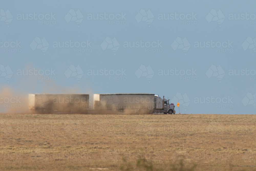 Heat ripples blurring prime mover pulling two curtain sided trailers on a dirt road - Australian Stock Image