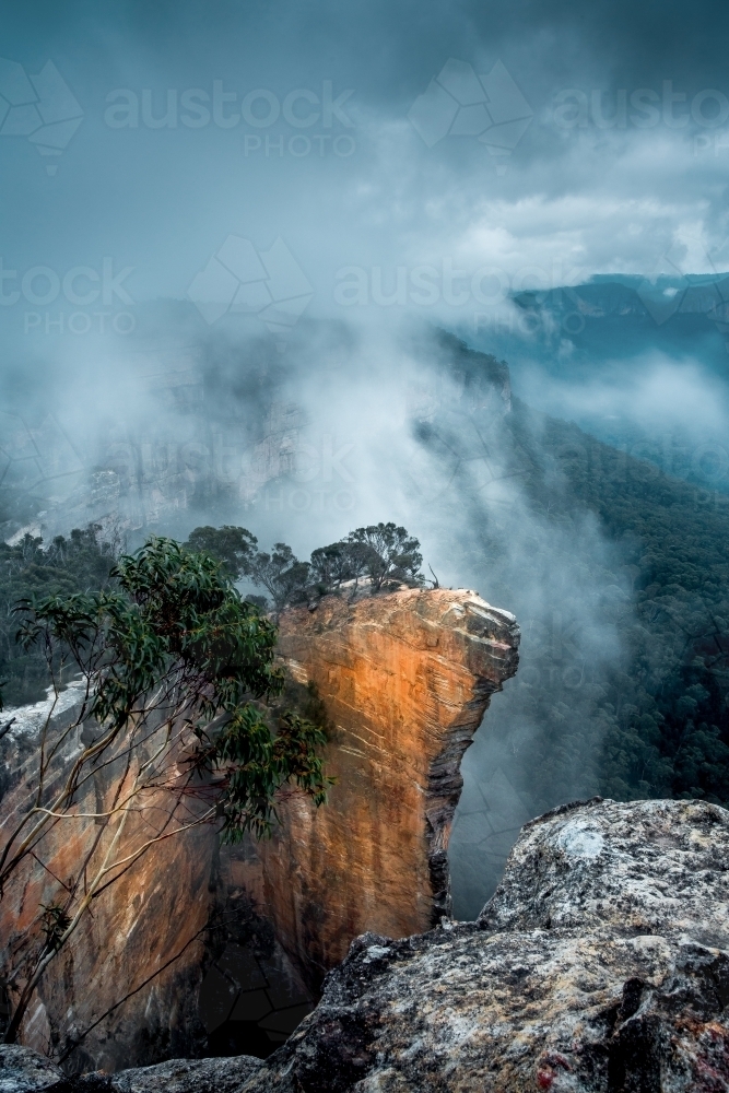 Heavy fog and mist emerge from the shrouded dark valleys to meet the sky.  Hanging Rock Australia - Australian Stock Image