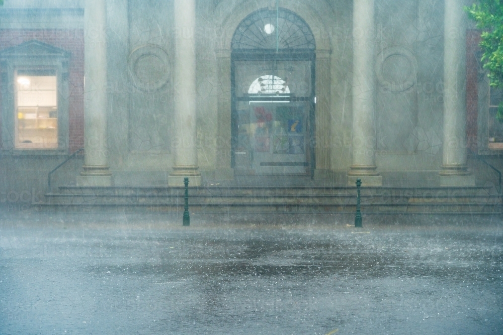 Heavy rain battering the facade of an historic buildings with prominent columns - Australian Stock Image