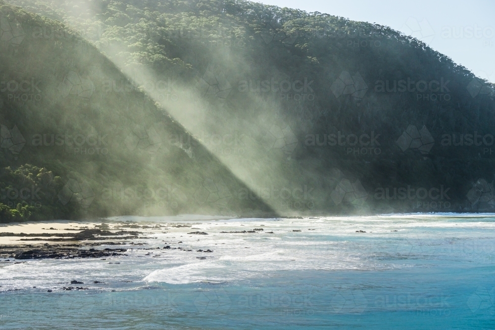 Heavy sea mist rising up a high coastline covered in trees - Australian Stock Image