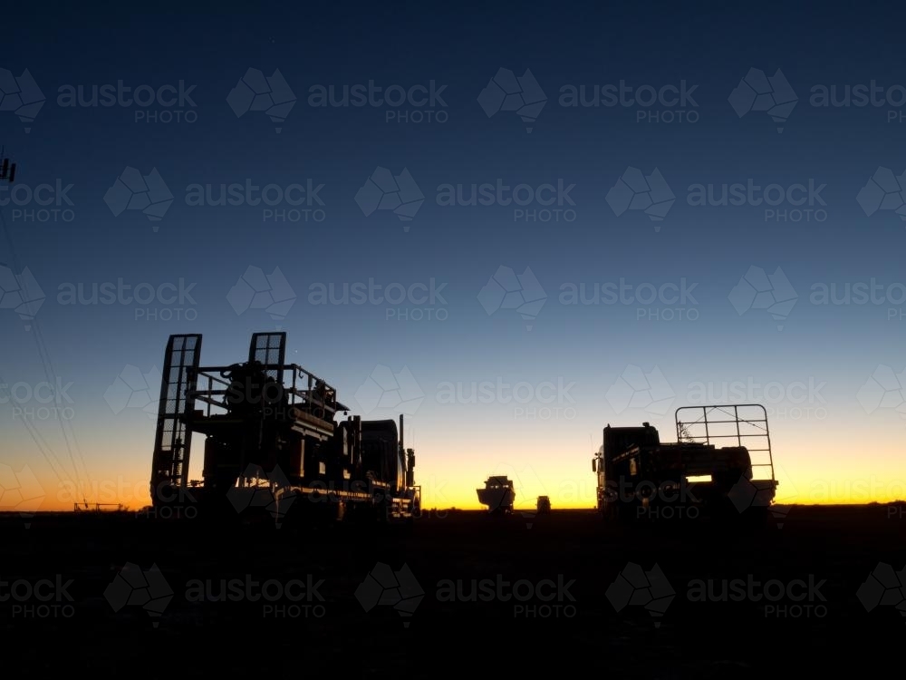Heavy vehicles silhouetted against a bright false dawn - Australian Stock Image