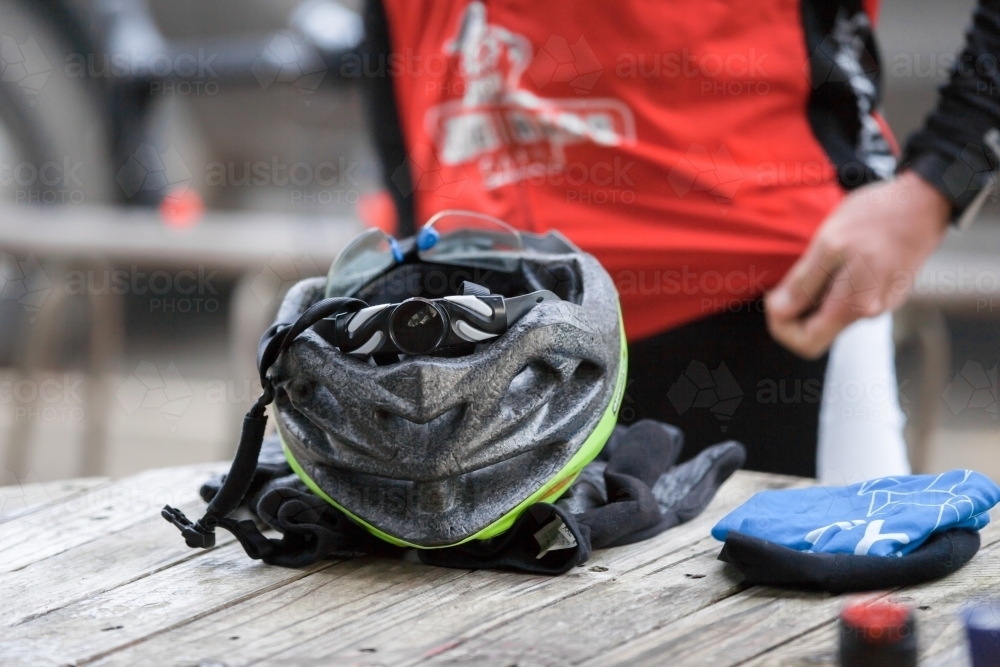 Helmet and gloves on a table at a cafe with a cyclist in background - Australian Stock Image