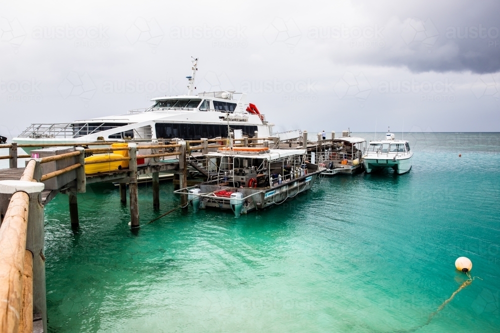 Heron Island jetty with several boats docked and grey skies - Australian Stock Image