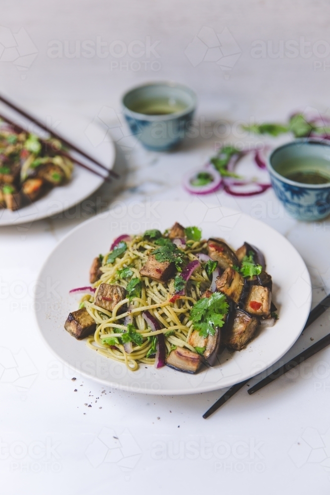 High angle of cold soba noodle, eggplant and parsley salad with green tea on white marble background - Australian Stock Image