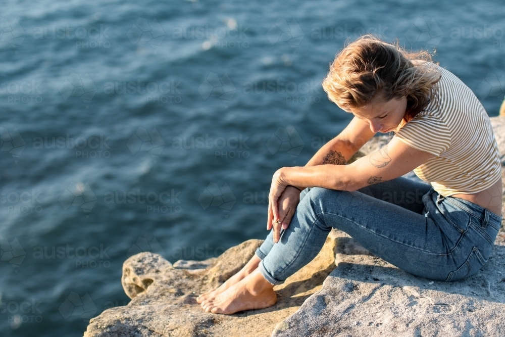 High angle shot of contemplative young woman sitting on clifftop above the ocean - Australian Stock Image