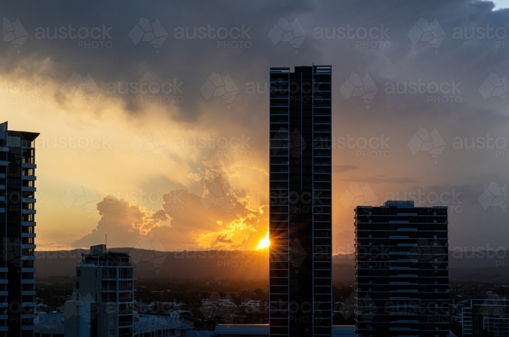 high rise buildings silhouetted against setting sun under stormy sky - Australian Stock Image