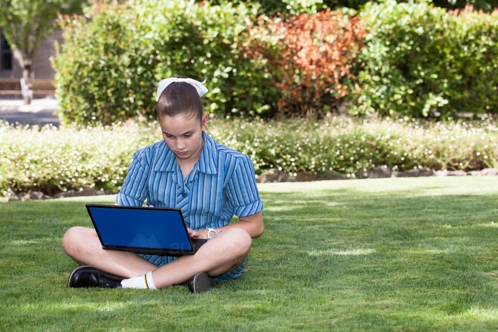 high school student working on laptop in the gardens - Australian Stock Image