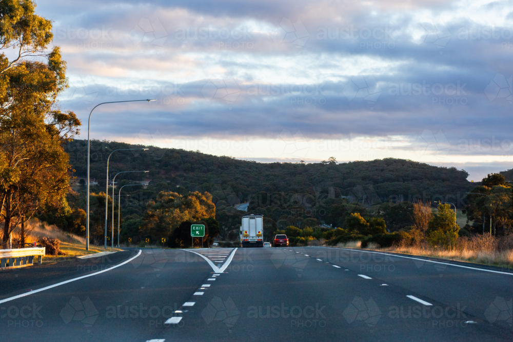 Highway at sunset drivers pov with exit sign on left - Australian Stock Image