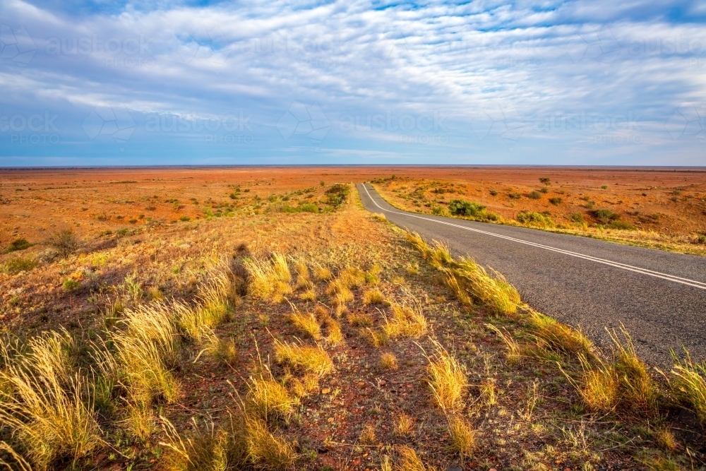 Highway through the desert landscape of outback Australia, rocky red soils, tufted grasses - Australian Stock Image