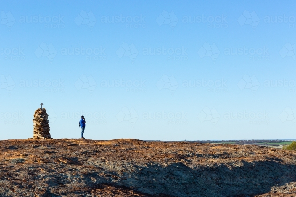 Hiker atop granite outcrop next to rock cairn - Australian Stock Image