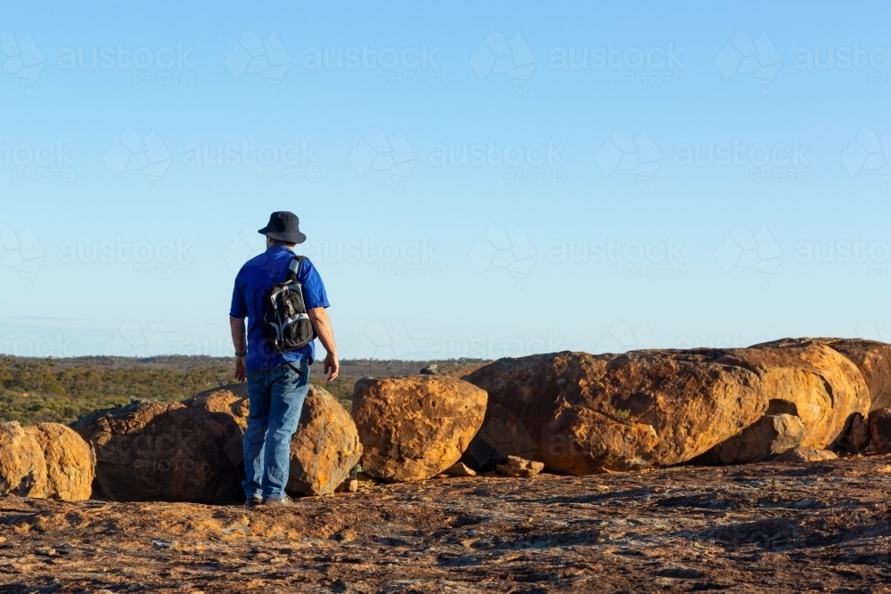 hiker looking towards the horizon near granite boulders - Australian Stock Image