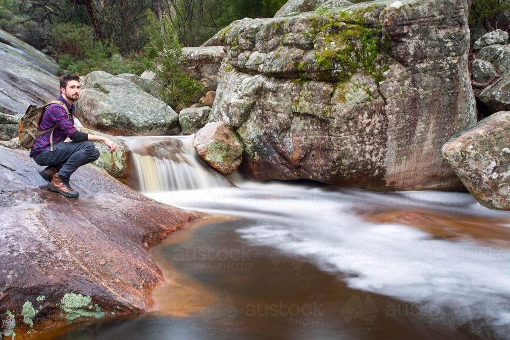 Hiker next to flowing rocky stream - Australian Stock Image