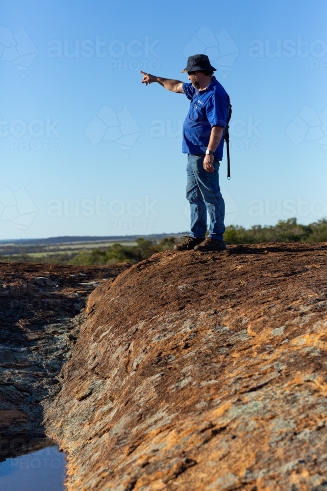 hiker on a rock pointing into the distance against a blue sky - Australian Stock Image