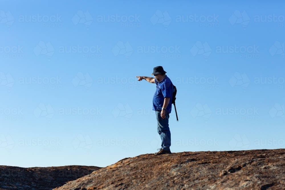 hiker on a rock pointing into the distance against a blue sky - Australian Stock Image