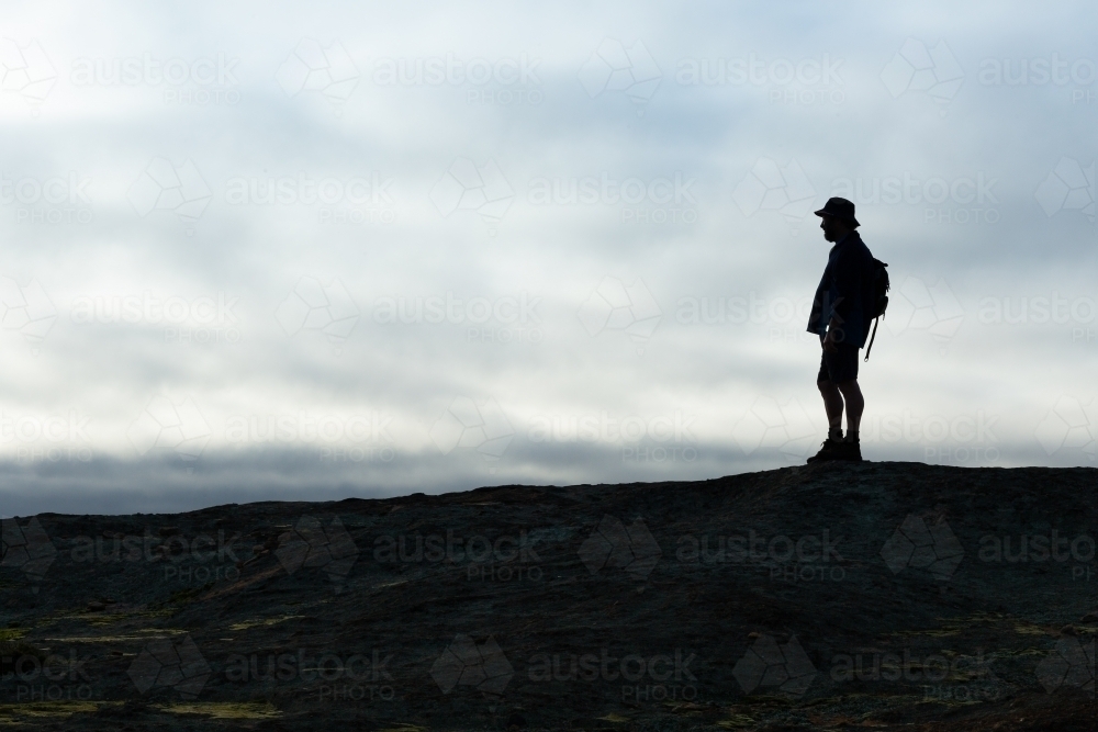 hiker silhouetted against cloudy sky in open landscape - Australian Stock Image