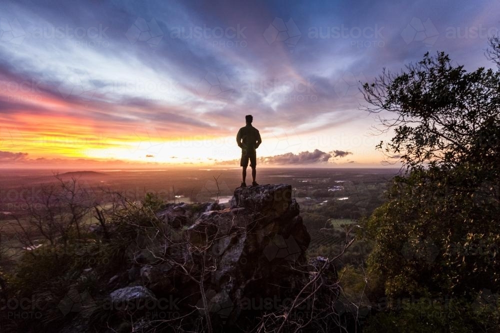 Hiker standing atop a rock formation watching sunrise from Mount Tibrogargan - Australian Stock Image