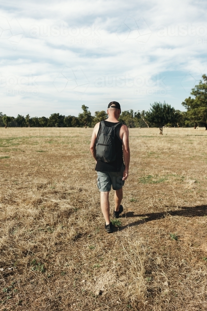 Hiker walking through a dry paddock of grass - Australian Stock Image