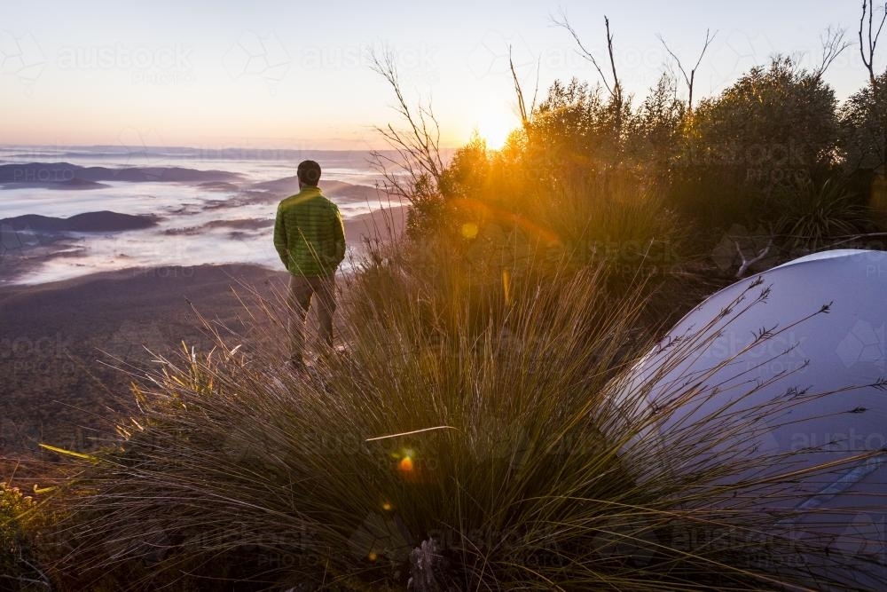 Hiker watching sunrise over misty valleys from Mount Barney - Australian Stock Image
