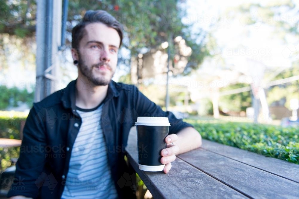 Hipster man sitting outdoors with a take away coffee - Australian Stock Image