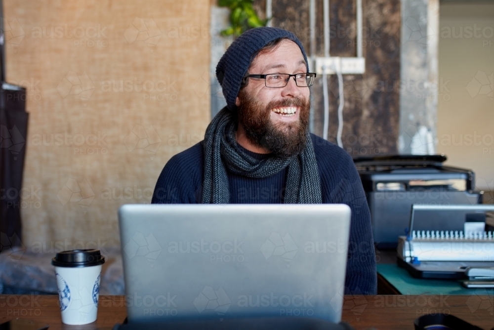 Hipster man with beard laughing at outdoor work table with a laptop - Australian Stock Image