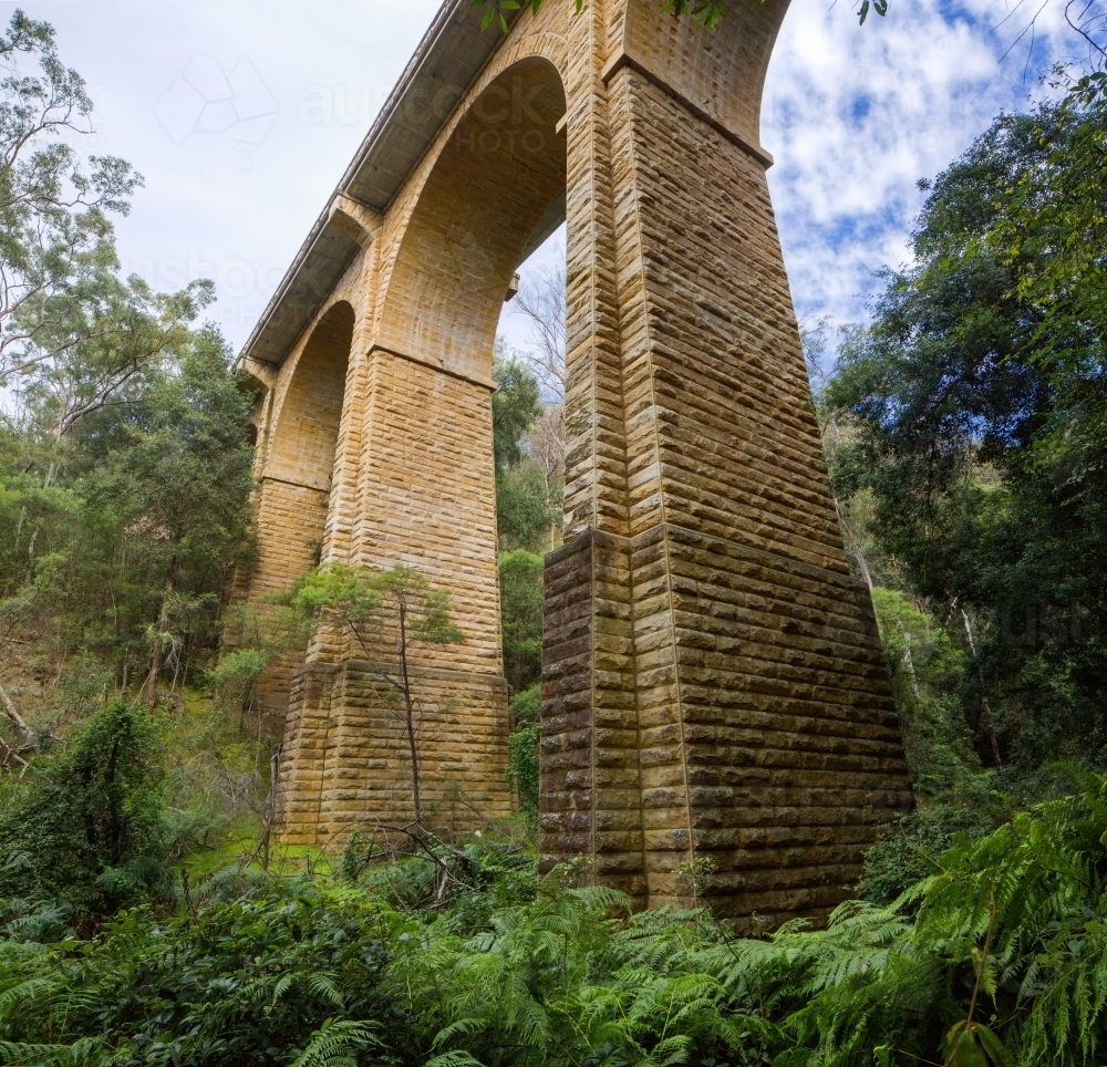Historic sandstone arch bridge from below, with green bush and clouds - Australian Stock Image