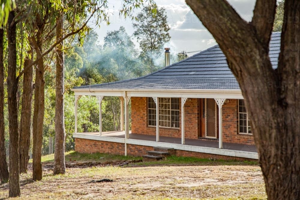 Home among gum trees with veranda and smoke drifting from chimney - Australian Stock Image