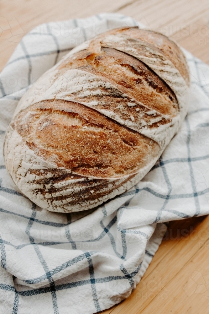 Home made Sour dough bread cooling on a tea towel which is on a wooden chopping board - Australian Stock Image