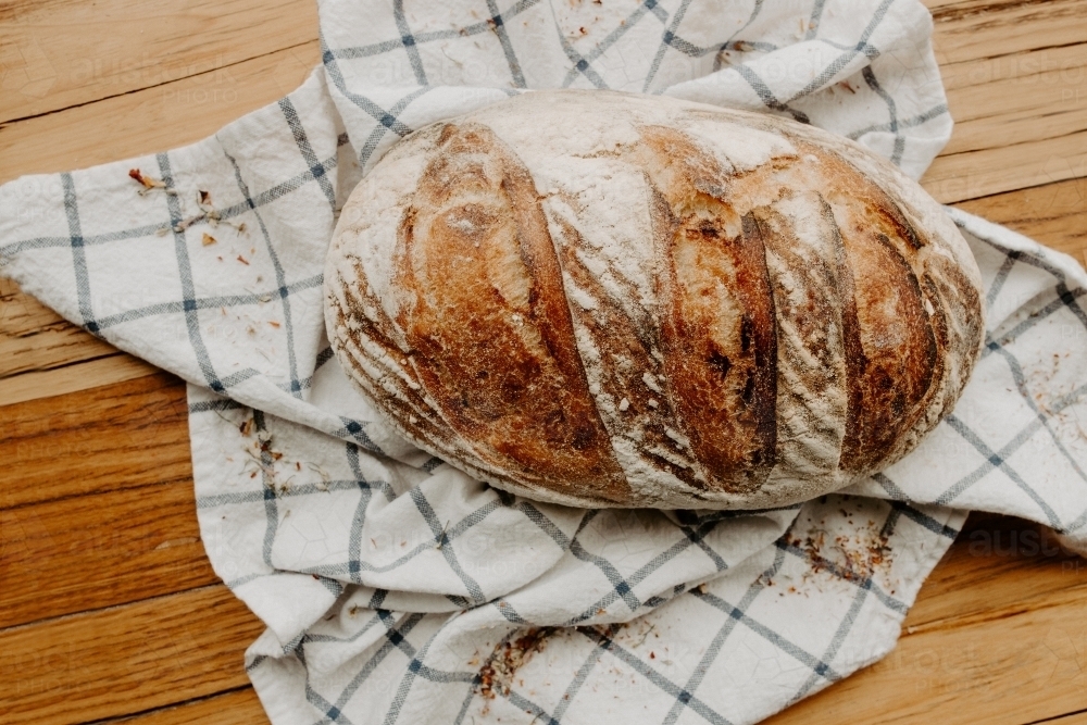 Home made Sour dough bread cooling on a tea towel which is on a wooden chopping platter board - Australian Stock Image
