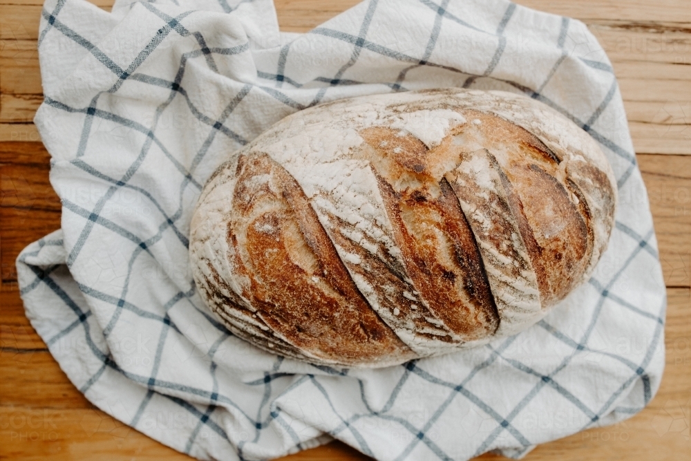 Home made Sour dough bread cooling on a tea towel which is on a wooden chopping platter board - Australian Stock Image