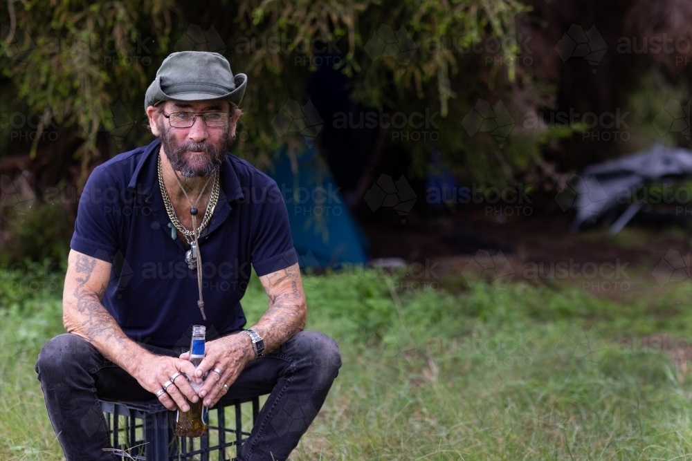 homeless man with a beer sitting on a milk crate in the bush - Australian Stock Image