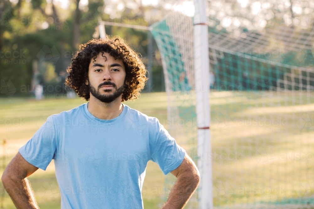 horizontal half body shot of a man with curly hair with arms in the side with goal in the background - Australian Stock Image