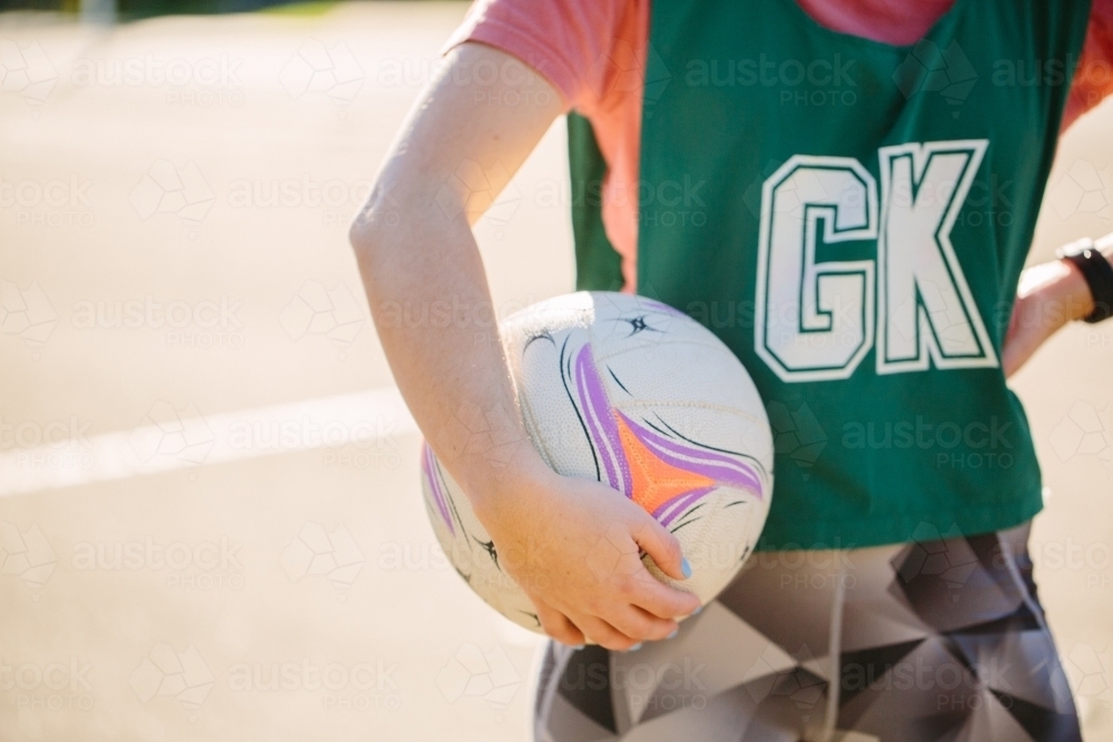 horizontal half body shot of a woman in sports wear holding a net ball in between her hand and waist - Australian Stock Image