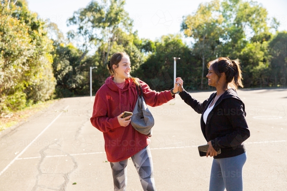 horizontal photo of two young women wearing coat and jacket holding each others hands on a sunny day - Australian Stock Image