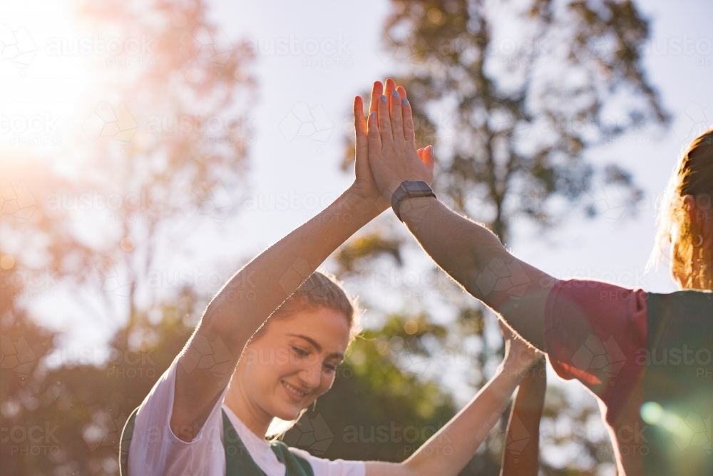 horizontal pic of a young woman giving high five to another woman on a sunny day - Australian Stock Image