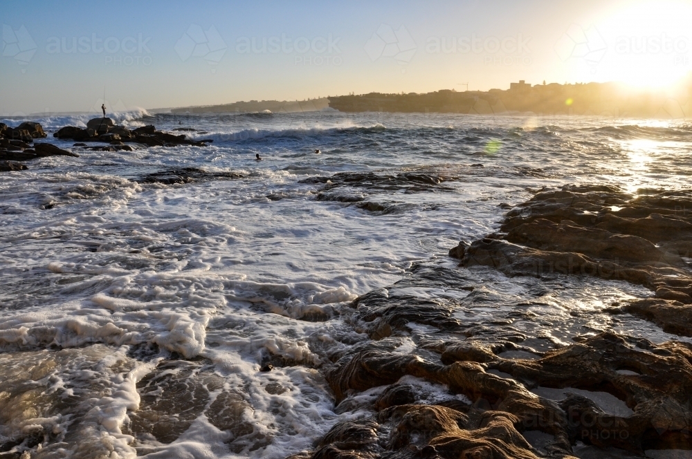 horizontal shot of a beach with waves, rocks and sunlight with clear skies - Australian Stock Image