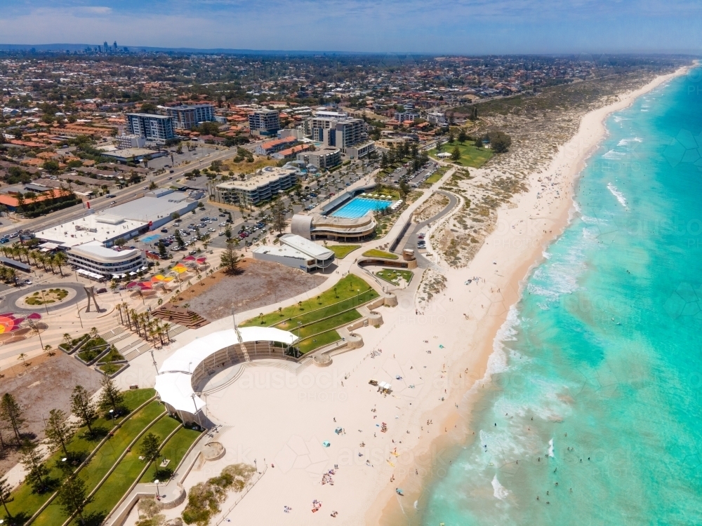 horizontal shot of a beach with waves, white sand, people swimming, grass, trees and buildings - Australian Stock Image