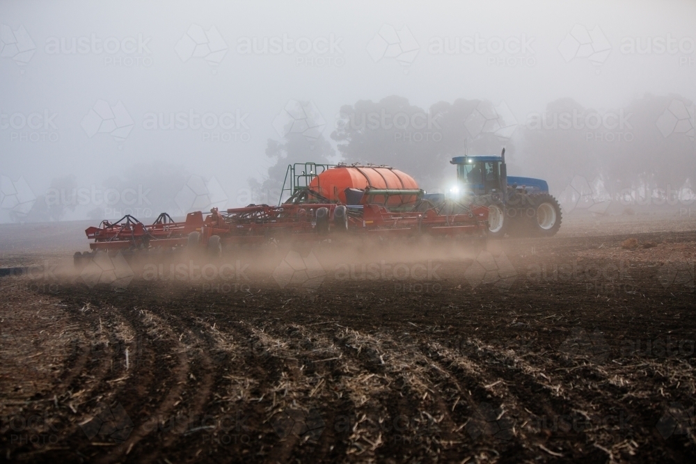 Horizontal shot of a blue tractor cultivating the soil in the field. - Australian Stock Image