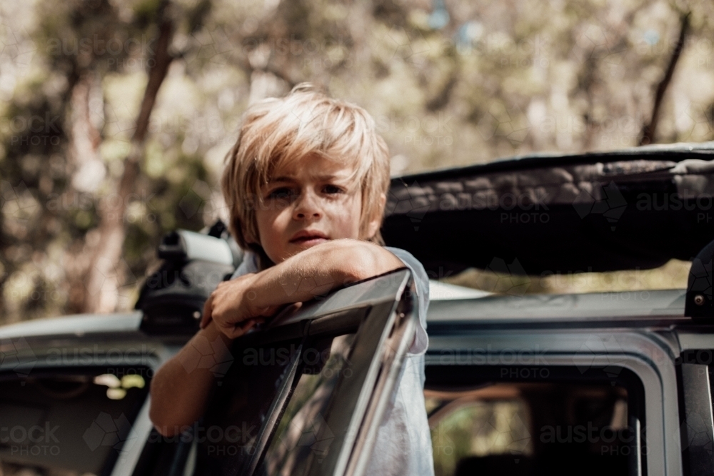 Horizontal shot of a boy leaning on the car door - Australian Stock Image