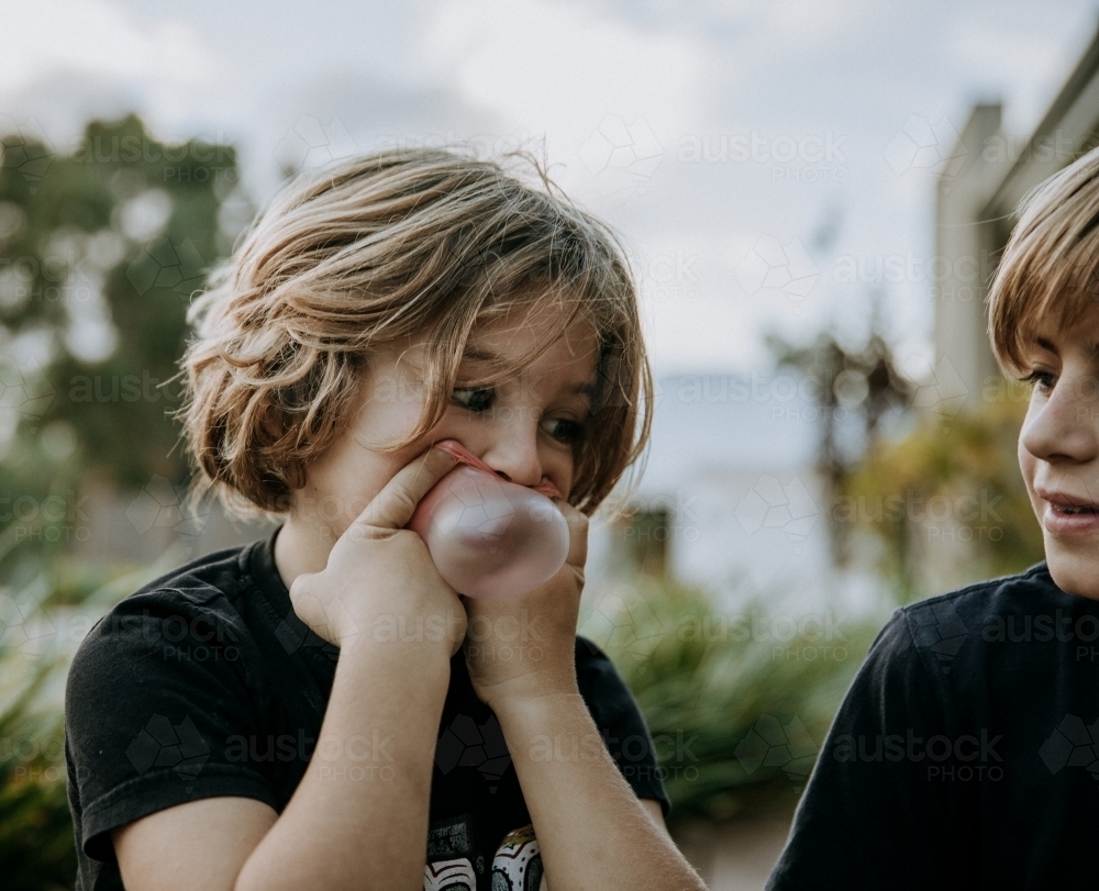 Horizontal shot of a boy watching a kid blow bubblegum - Australian Stock Image