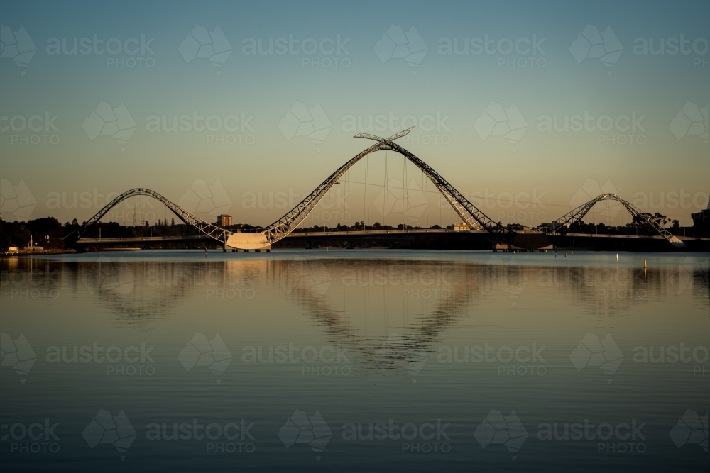 horizontal shot of a bridge with wavy structures reflecting in a body of water with clear skies - Australian Stock Image