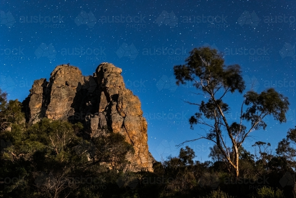 Horizontal shot of a brown rocky mountain under blue sky during night time - Australian Stock Image