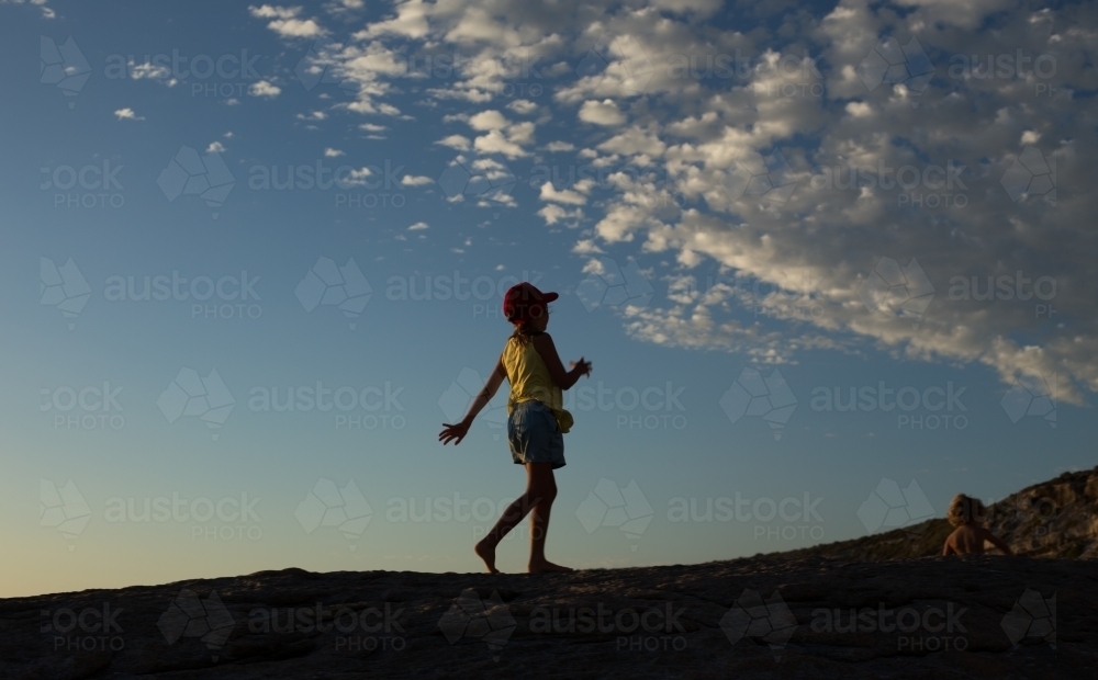 Horizontal shot of a child walking along hilltop at dusk - Australian Stock Image