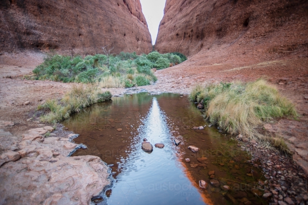 Horizontal shot of a creek with two large rock formation in the background - Australian Stock Image
