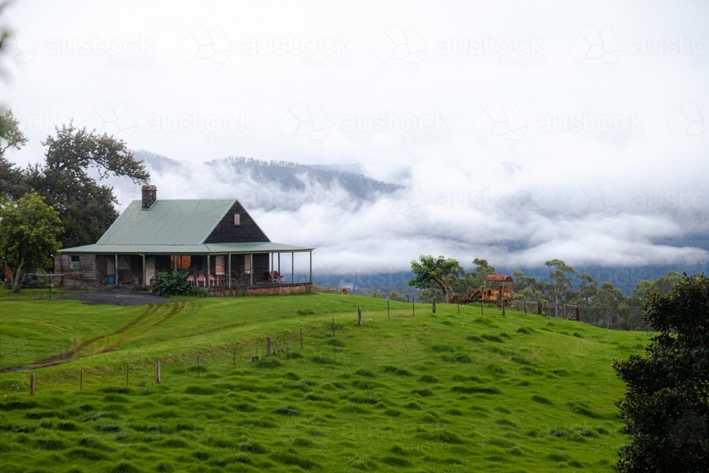 horizontal shot of a house with green lawn and foggy mountains in the background - Australian Stock Image
