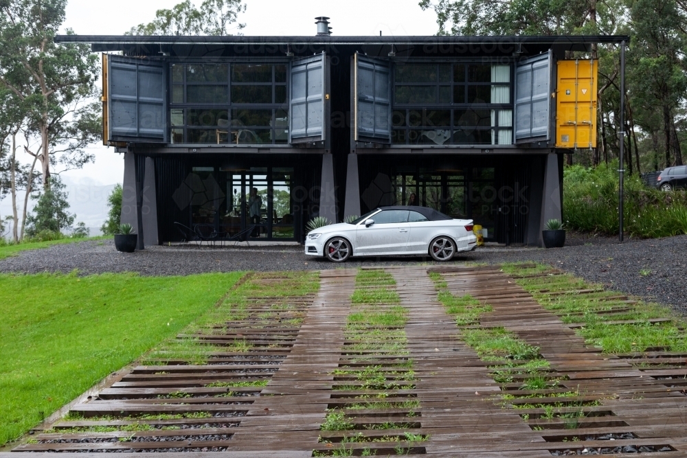 horizontal shot of a house with open windows, white car and wet ground with green grass - Australian Stock Image