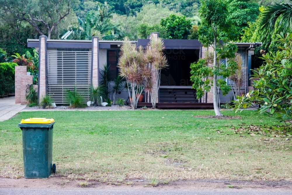 horizontal shot of a house with trees, grass and a trash bin in front - Australian Stock Image