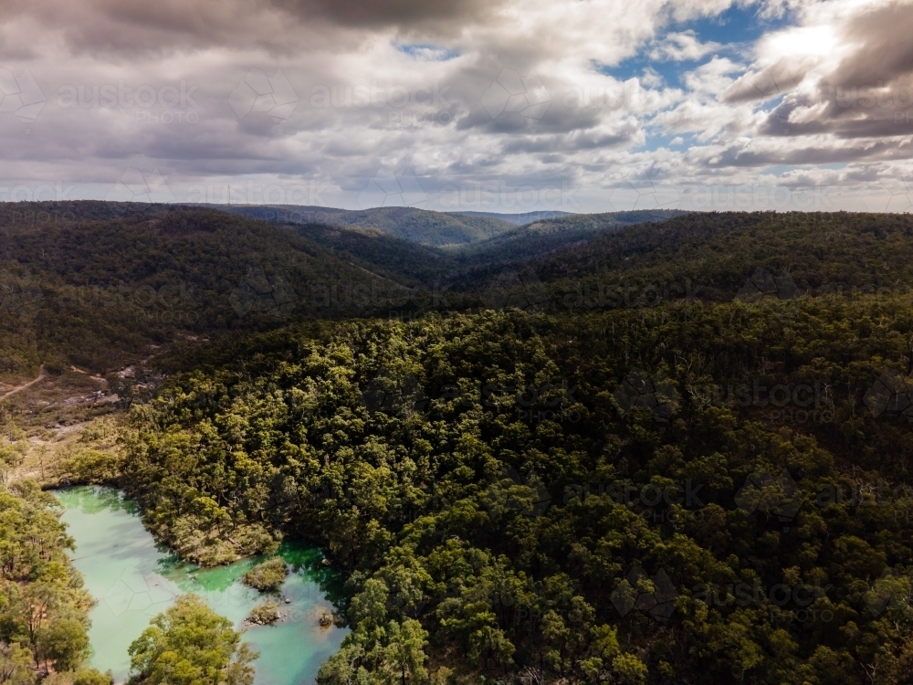 horizontal shot of a lake surrounded by bush hills with green trees on a cloudy day with grey skies - Australian Stock Image