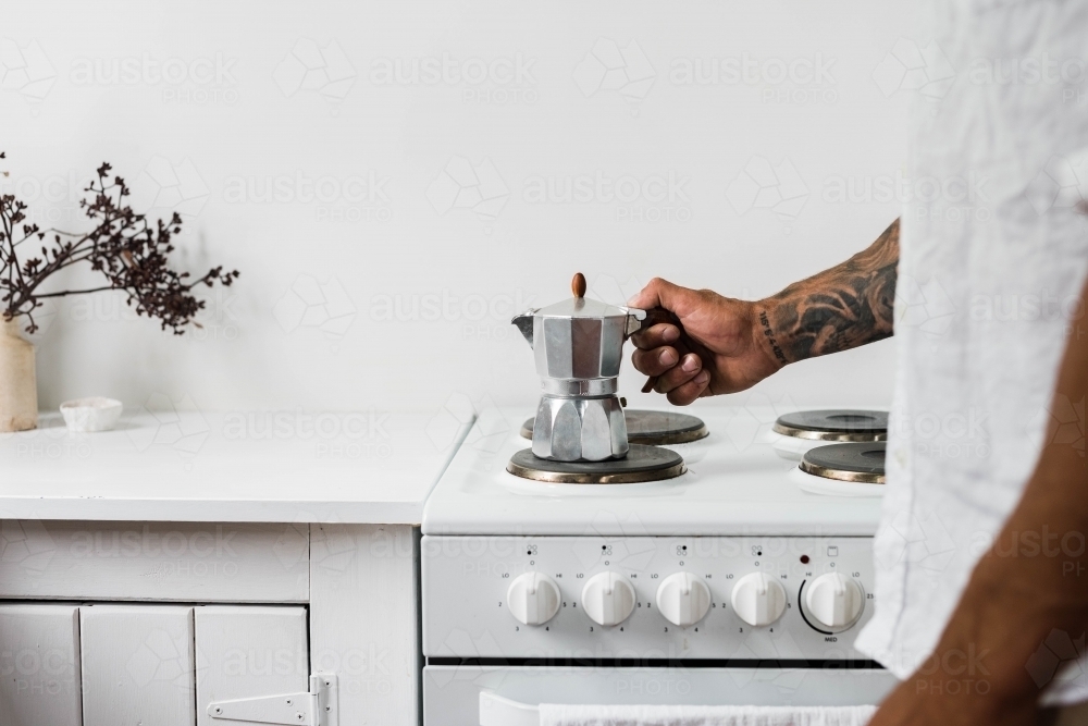 Horizontal shot of a man's hand holding a coffee maker on a stovetop burner - Australian Stock Image