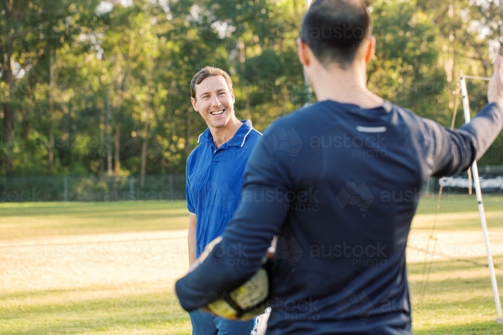 horizontal shot of a man smiling in the field on a sunny day with another man holding a soccer ball - Australian Stock Image
